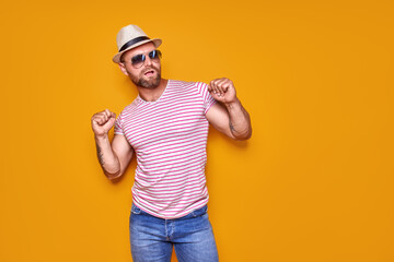 Portrait of optimistic funky guy dance wear summer look straw hat, sunglasses isolated on yellow color background