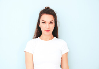 Obraz premium Closeup portrait of young beautiful smiling female in trendy summer white t-shirt. Sexy carefree woman posing near light blue wall in studio. Positive model having fun indoors. Cheerful and happy