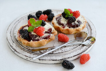 Close-up of delicious muffins with berries and mint leaves on a wooden plate on a light background