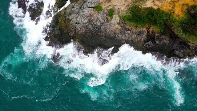 The view from the top-down drone on the Andaman Sea coast, huge seas crashing into the shores filled with black mountain rocks.