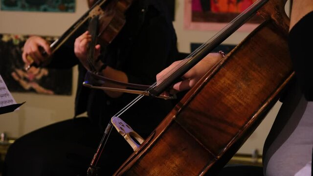Cinematic close up shot of symphony orchestra with performers wearing medical protective masks playing violins and cello on classic theatre with curtain stage during music concert.