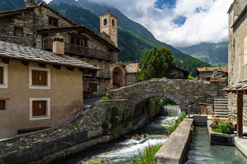 Fototapeta na wymiar The charming village of Chianale in the heart of the Alps, with a picturesque river passing under stone bridge, Italy