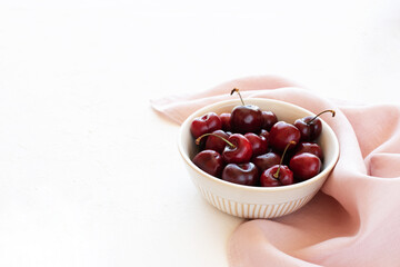 Raw cherries in a bowl on a pink napkin and white background