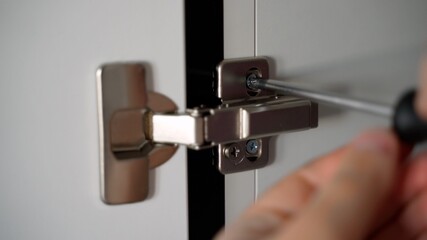 The man unscrews the screw with a screwdriver. Customization of hardware in metal color silver chrome furniture hardware. White wooden door. Close-up
