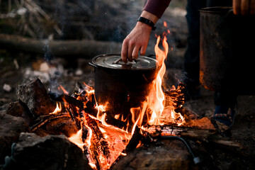 man's hand holds the lid of saucepan that stands on burning fire - obrazy, fototapety, plakaty