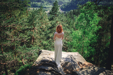 beautiful young red-haired bride in the forest with a floral wreath on her head. woman in long...