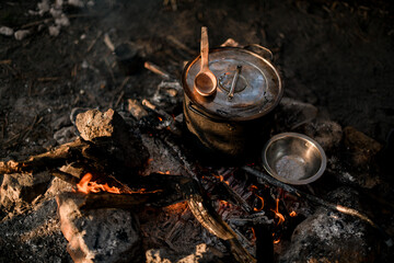 bowl and saucepan and wooden spoon on the wood of campfire