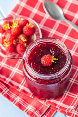 Red rasberries jam in jar and ripe raspberries.