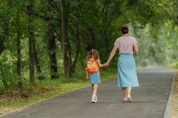 friendly family goes to kindergarten. woman morally supports daughter, holding hands, encourages...