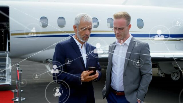 Network of profile icons against two caucasian businessmen using smartphone at airport runway