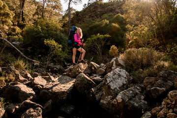 Great view of beautiful woman with backpack and trekking poles standing on stone