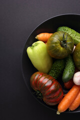 Black plate variety of raw vegetables ready to cook fresh natural vegetables on black background.