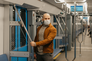 Fototapeta na wymiar A bald man with a beard in a face mask is holding the handrail in a subway car.