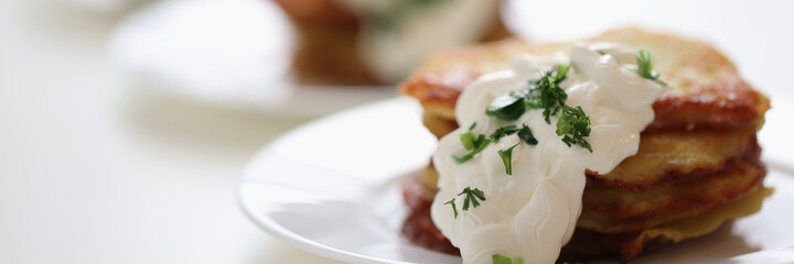 Appetizing potato pancakes with sour cream sauce and dill lying on plate