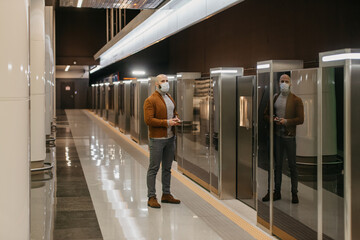 Fototapeta premium A man in a face mask is holding a smartphone while waiting for a subway train.
