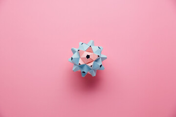 Multicolor handmade modular origami ball or Kusudama Isolated on pink background. Visual art, geometry, art of paper folding, paper crafts. Top view, close up, selective focus, copy space.