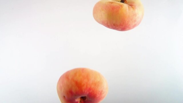 Closeup 4k footage of donut peaches falling in water against white backgorund.