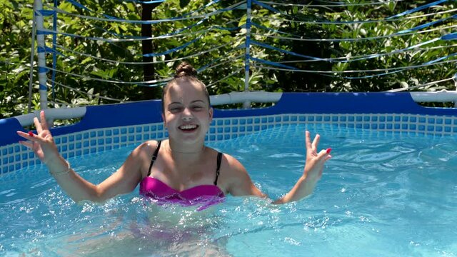 Happy girl child swim in outdoor swimming pool showing v sign victory hand gesture, summer