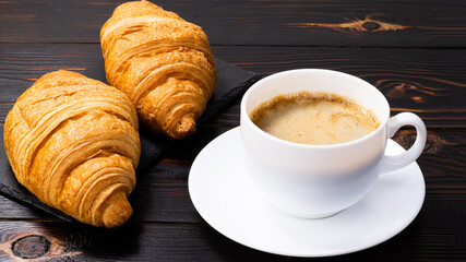 cup of coffee and croissant on wooden table. Top view