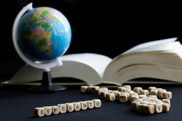 Inscription esperanto next to an open book, Latin letters and a small globe. The concept of learning and using the Esperanto language. Dark background. Macro. Selective focusing