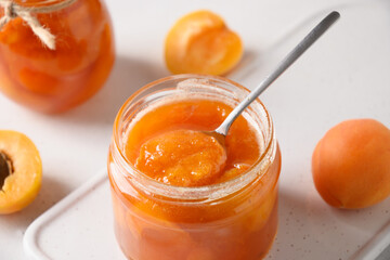 Apricot jam in open glass jar with fruits on white background. Summer harvest and canned food for winter. Tasty dessert. Close up.