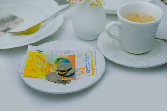 close-up of white plate for money, Swiss francs banknotes and coins, Restaurant bill, cup of coffee, delicate pink flowers, dishes with food, the concept of tip money, change of the waiter