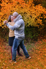 aged man and woman have fun dancing in the autumn park against the background of trees, the concept...