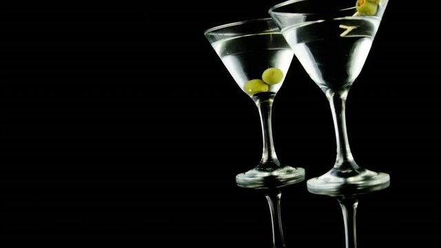 Animation of confetti falling over cocktail glasses of wine and olives on black background