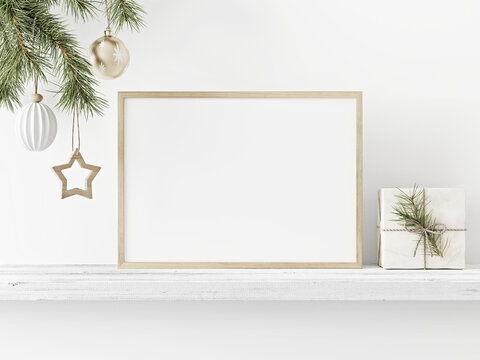 Small horizontal wooden frame mockup with hanging pine branch and gift box on shelf on empty white wall background. Minimal Christmas interior decoration. A4, A3 format. 3d rendering, illustration