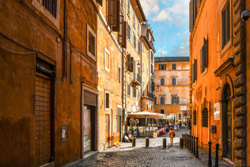 A colorful empty alley leading to a sidewalk cafe and small piazza in the historic center of Rome, Italy