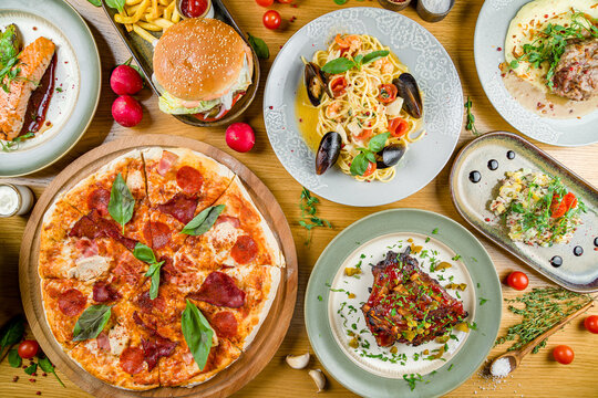 Italian meat pizza, salmon steak with avocado, spaghetti with shrimps and mussels, burger with meat,  pork reabs bbq, salad olivier, beef cheaks top view on wooden table