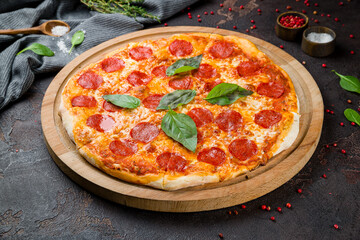 Pepperoni pizza with basil on wooden board on dark concrete table