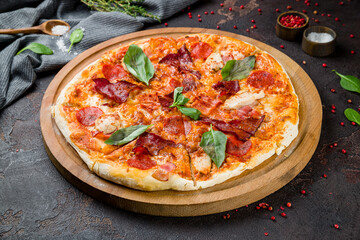 Italian meat pizza with chicken, ham, basil and cheese on the board on dark concrete table