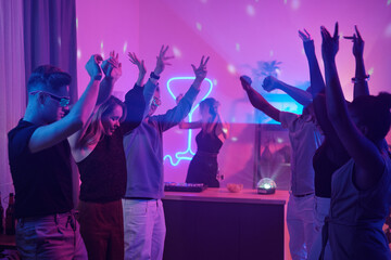 Young intercultural friends in casualwear raising arms while dancing together