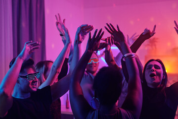 Obraz na płótnie Canvas Young intercultural glamorous friends raising their arms while dancing at party