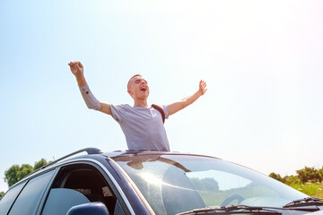 Young caucasian man with an amputated arm and prosthesis stands with raised arms waist-deep from the hatch of a car and shout. Freedom, independence concept