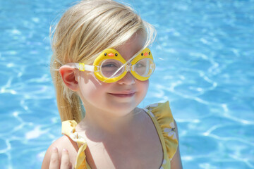 Portrait of toddler girl wearing swimming goggles with clear blue water background