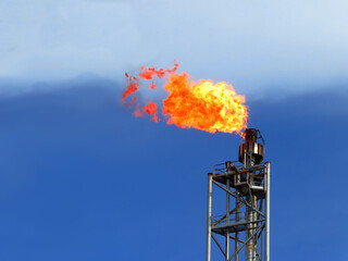 Gas flare is releasing and burning to the atmosphere at an offshore gas platform with sky. Fire on...