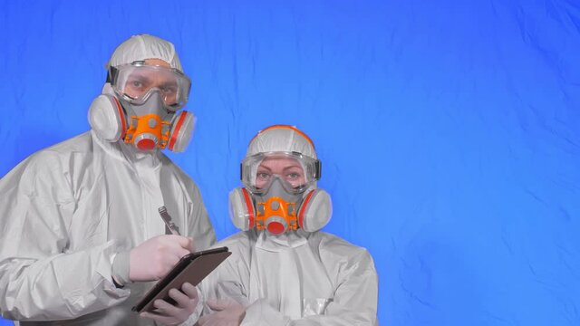 Scientist virologist in respirator makes write in an tablet computer with stylus. Man and woman wearing protective medical mask. Health safety virus coronavirus epidemic 2019 nCoV. Chroma key blue.