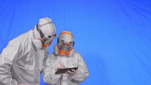 Scientist virologist in respirator makes write in an tablet computer with stylus. Man and woman wearing protective medical mask. Health safety virus coronavirus epidemic 2019 nCoV. Chroma key blue.
