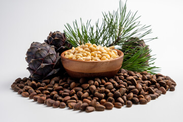 Pine nuts in wooden bowl with cones on white background