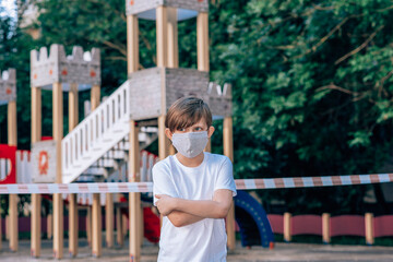 Obraz premium portrait of upset boy in mask, background closed playgrounds in the city.