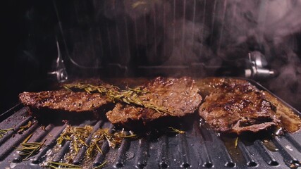 Delicious juicy meat steak cooking on grill. Aged prime rare roast grilling tenderloin fresh marble tenderness beef. Prime beef fry on electric roaster, rosemary, black pepper, salt. Slow motion.