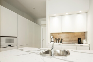 Fototapeta na wymiar Open plan kitchen with island and gray veined marble sink and white cabinets in a vacation rental apartment