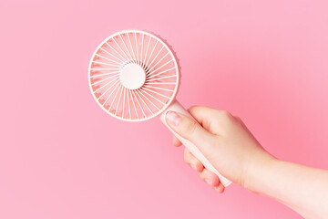 Female hand holding a small fan on pink background close-up. © TATIANA KIM