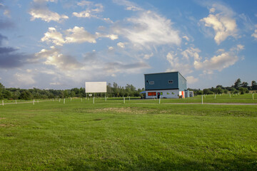 Empty rural drive -in theatre, daytime, nobody, grass parking spots, white posts, screen,...