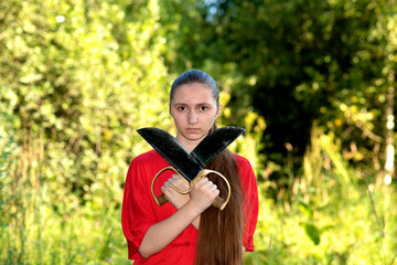 Close up portrait  . A 
beautiful teen girl sportswoman athlete engaged in Wushu outside, in red sport kung fu costume, training  with traditional wing chun sport knives butterflies