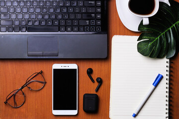 top view, wooden office desk with laptop, notebook, a cup of coffee, pen, smartphone, green leaf, glasses, 
earphones, and space for your creations.