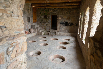 Old wine cellar in ancient Nekresi monastery with qvevris buried in stone floor and wooden trough for trampling grapes, Georgia