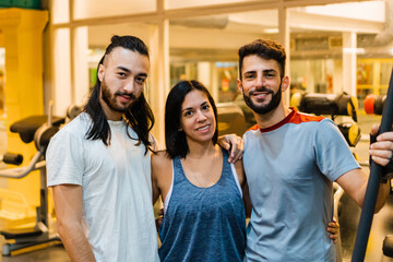 three athletes in a gym looking at the camera, hispanic latina woman, men, smiling hugging each other